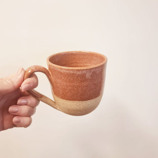 Hand holding a pink ceramic mug against a plain background