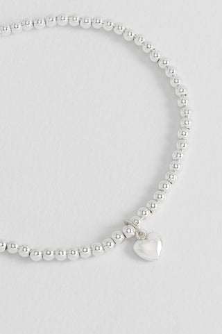 Silver beaded bracelet with a heart charm on a light gray background