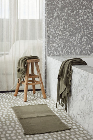 Bathroom with a wooden stool, green towel, and patterned rug.