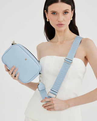 Woman holding a light blue handbag with a matching strap against a white background