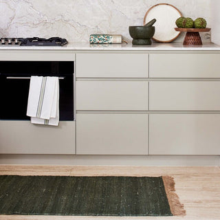 Modern kitchen with light gray cabinets, black oven, and green rug on wooden floor.