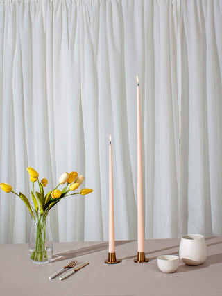 Decorative table setting with candles, flowers, and cutlery against a white curtain background.