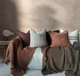 Cozy living room scene with pillows and blankets on a sofa against a textured wall.