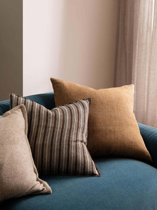 Three pillows on a blue sofa against a neutral wall.