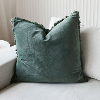 Green velvet pillow with frayed edges on a light-colored sofa.