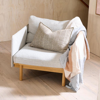 Light gray armchair with wooden legs, beige pillow, and blanket on a wooden floor.