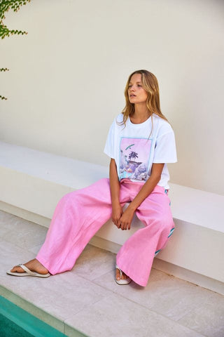Woman sitting on a ledge wearing a white t-shirt with a graphic design and pink pants.