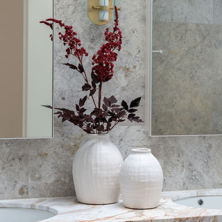 Two white vases with dried red flowers on a marble countertop in a bathroom.