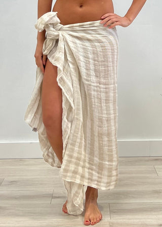 Person wearing a light-colored, patterned sarong on a plain background