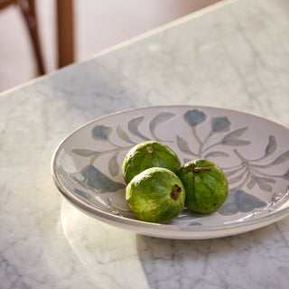 Three green fruits on a decorative ceramic plate with floral patterns on a marble surface.