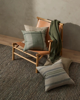 Wooden chair with cushions and a blanket on a textured floor against a neutral wall.