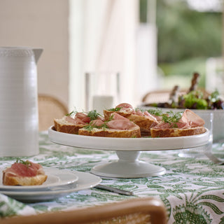 Plated appetizers on a white cake stand with a blurred outdoor setting