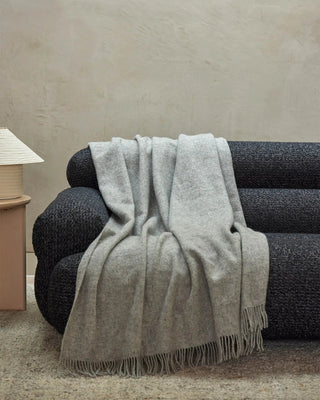 Gray throw blanket draped over a black sofa against a beige wall.