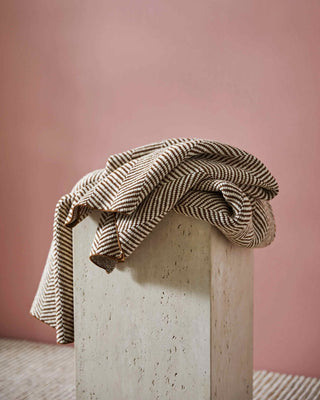 Textured blanket draped over a concrete block against a pink wall