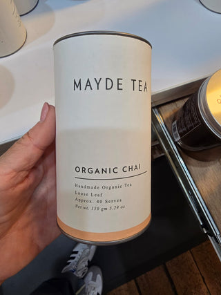 Mayde Tea Organic Chai canister held by a hand on a kitchen counter.