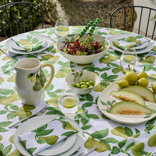 Dining table set with a green leafy tablecloth, fruit-themed plates, and a bowl of salad.