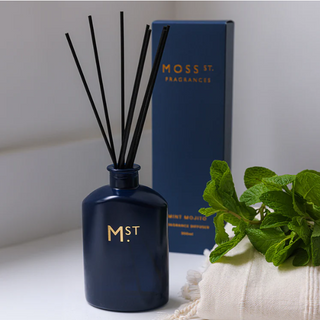 Navy blue diffuser with black sticks and 'Moss St. Fragrances' branding on a light background.