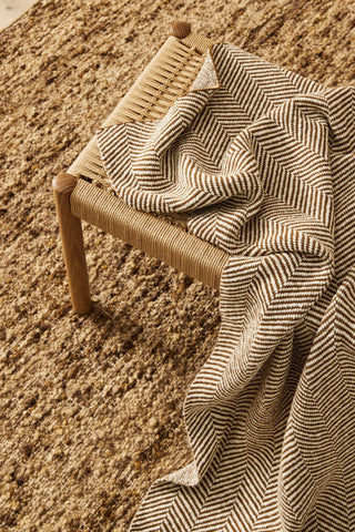 Woven chair with a striped fabric draped over it on a textured surface