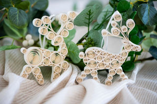 Two decorative paper reindeer on a white fabric background with green leaves.