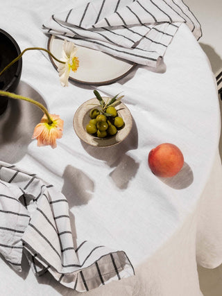 Table setting with a bowl of olives, peach, and striped cloth on a white tablecloth.