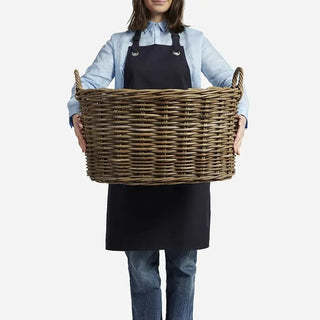 Person holding a large wicker basket wearing an apron on a white background