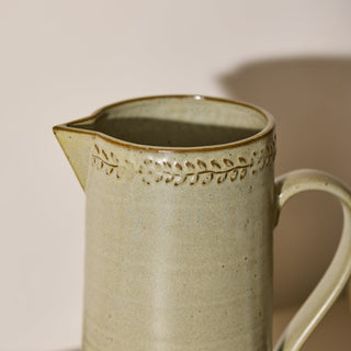 Stoneware pitcher with decorative rim on a beige background
