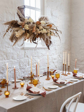 Elegant table setting with candles, flowers, and decorative items against a white brick wall.