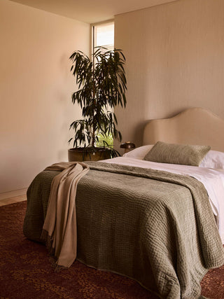 Bedroom with a bed, plant, and window in a warm-toned room.