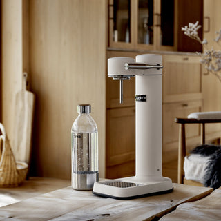 White soda dispenser on a wooden table with a bottle of Sodastream in a kitchen setting.