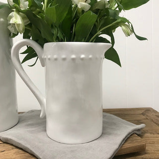 White ceramic pitcher with floral arrangement on a wooden surface