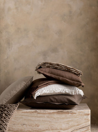 Stack of brown pillows and blankets on a wooden surface with a beige background