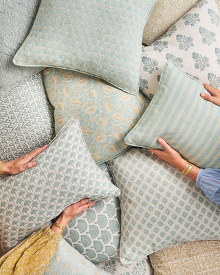 Collection of patterned cushions being held by hands on a neutral background