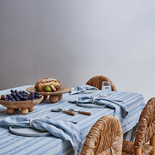 Dining table with a blue and white striped tablecloth, wooden bowl with berries, and wicker chairs.