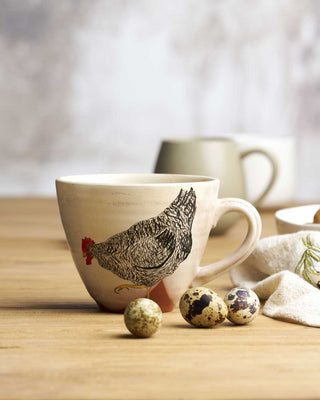 Ceramic mug with chicken design on a wooden surface with quail eggs.