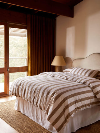Bedroom with striped bedding and a lamp next to a window