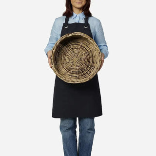 Person wearing a black apron holding a woven basket on a white background