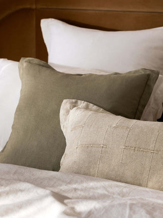 Close-up of textured pillows on a bed with a wooden headboard.
