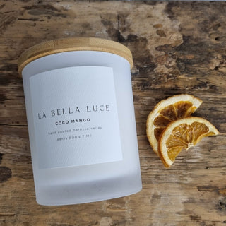 Candle with 'La Bella Luce' label on a wooden surface with orange slices