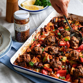 Baked dish with meatballs and vegetables on a table with a jar of seasoning.