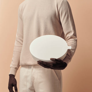Person holding a white, oval-shaped object against a beige background
