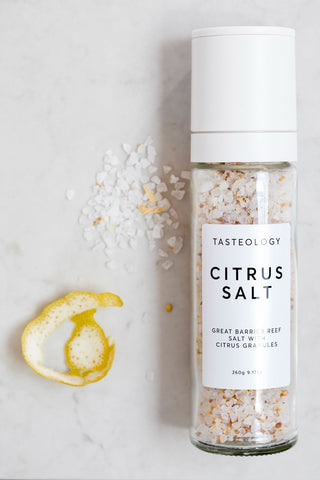 Bottle of Tasteology Citrus Salt on a light background with a lemon peel.