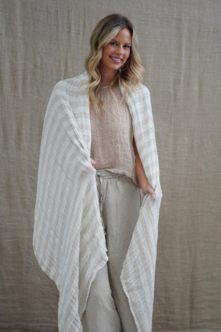 Woman wearing a light-colored striped shawl over a beige outfit against a neutral background