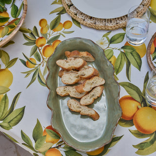Green ceramic dish with bread slices on a tablecloth with lemon pattern