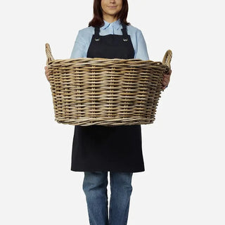 Person holding a large wicker basket against a plain background
