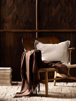 Wooden chair with a brown blanket and white pillow against a wooden paneled wall.