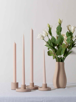 Set of pink candles in holders with a vase of flowers on a white surface.