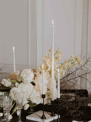 Table setting with white flowers, candles, and glassware against a neutral background