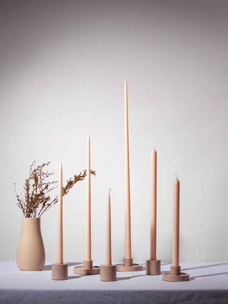 Set of tall, thin candles in beige holders on a neutral background
