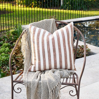 Striped pillow on a decorative chair outdoors with a garden background