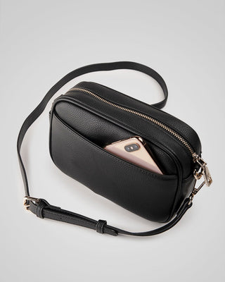 Black crossbody bag with a phone inside on a light gray background